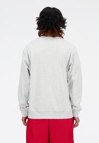 Sweatshirt gris clair à manches longues, avec col et poignets côtelés, présenté de dos. Associé à un short rouge. Le tissu semble doux.