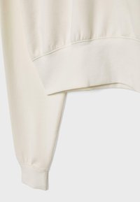 Manche de sweat-shirt couleur crème et bas avec poignets côtelés sur un fond clair uni.