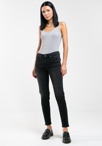 Jeans negros de cintura alta con corte ajustado, confeccionados en denim. Combinados con una camiseta gris ajustada y zapatos negros gruesos. Diseño minimalista.