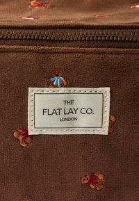 Ruskea kangaspussi vetoketjulla, jossa on kirjailtuja nallekarhuaiheita eri väreissä. Tunnuksessa lukee "THE FLAT LAY CO. LONDON."