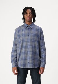 Button-up skjorte i et blått rutemønster med krage, lange ermer og en avslappet passform. Laget av et teksturert stoff med knappelukking.