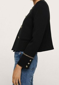 Czarna krótka kurtka z guzikami w złotym odcieniu, dopasowanym krojem i gładką fakturą; posiada subtelny pasek na rękawach.