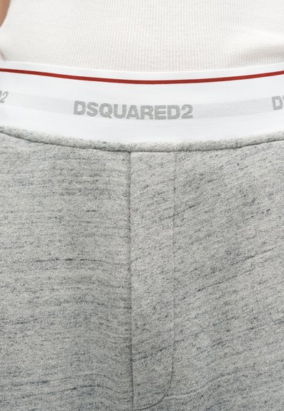 Κοντινό πλάνο της μέσης γκρι φόρμας με λευκή ελαστική ταινία που φέρει το λογότυπο "DSQUARED2" και ένα άτομο που φοράει λευκό ριμπ μπλουζάκι.
