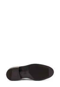 Sole di scarpa in pelle nera con superficie strutturata, forma arrotondata e arco prominente. Dettaglio di cucitura lungo i bordi.