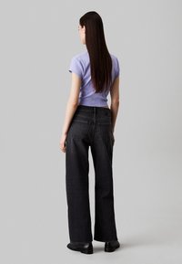Jeans negros de pierna ancha y una camiseta ajustada de manga corta en color lila, con una textura suave, silueta recta y bolsillos traseros visibles.