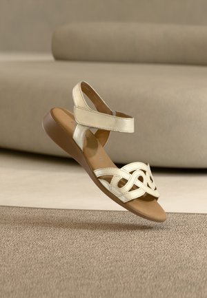 Gouden metalen sandaal met een open teen, verstelbare bandjes en een decoratief uitgesneden ontwerp. Gewatteerde bruine zool, platte hak.