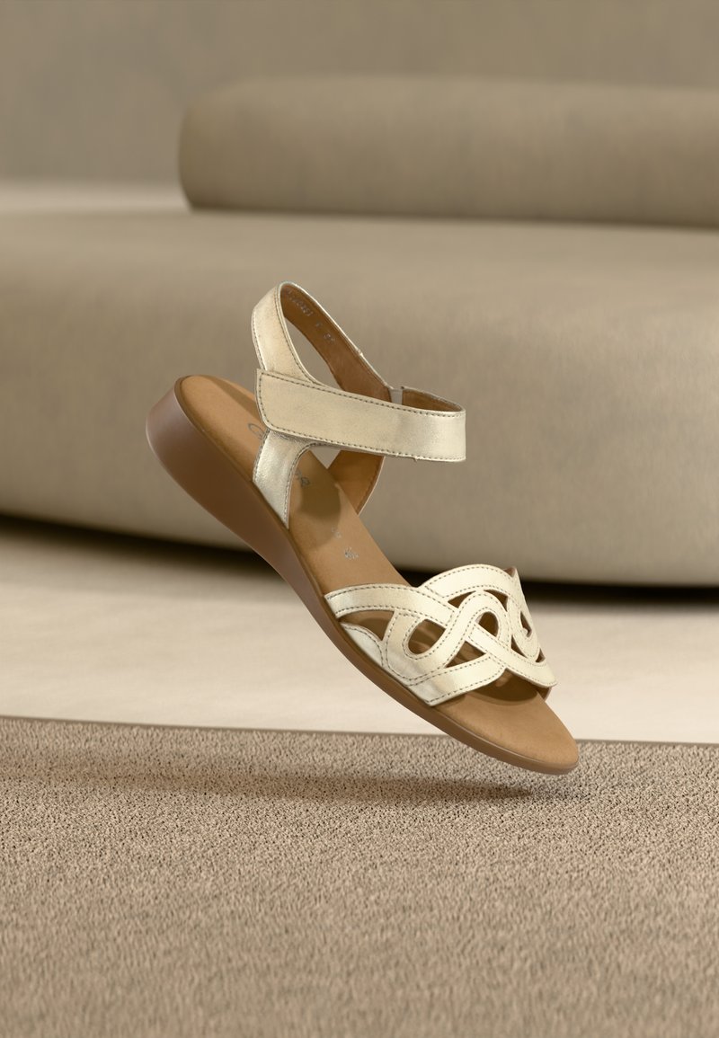 Χρυσό μεταλλικό σανδάλι με ανοιχτά δάχτυλα, ρυθμιζόμενα λουριά και διακοσμητικό σχέδιο με κοψίματα. Μαλακή σόλα σε καφέ χρώμα, επίπεδη φτέρνα.