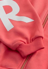 Koralas zip-up kapuce, kas aprīkota ar lielu baltu "R" logo, ribotām piedurknēm un gludu tekstūru. Zelta rāvējslēdzējs piešķir metāla akcentu.