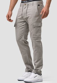 Helle graue Cargo-Hosen mit seitlichen Taschen, einem lässigen Schnitt und einem Kordelzugbund. Getragen mit weißen Sneakers und einem schwarzen Bund.