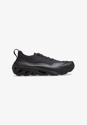 Chaussure de sport noire dotée d'une tige en maille et d'une semelle en caoutchouc texturée avec des découpes, conçue pour un confort et une adhérence améliorés.