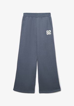 Pantaloni da tuta larghi blu con vita elastica, tasche laterali, strisce bianche sui lati e numero "82" bianco sulla parte superiore della gamba sinistra.