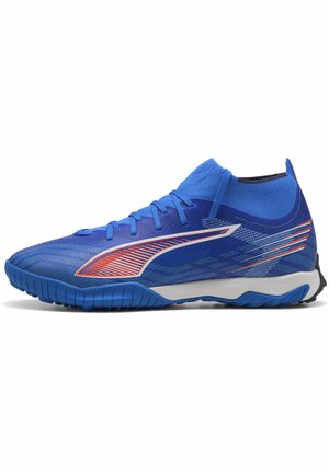 Blauwe sportieve schoen met hoge kousachtige kraag, oranje en witte zijlogo, textuurzool en veters op een witte achtergrond.
