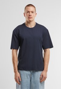 Tricou cu maneci scurte, de culoare bleumarin, din bumbac moale, cu guler rotund și croială lejeră, asociat cu pantaloni scurți de denim deschis, cu croială largă.