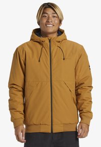 Chaqueta de capucha marrón con cremallera al frente, puños elásticos y dos bolsillos laterales; presenta una textura suave y elegante, ideal para uso al aire libre.