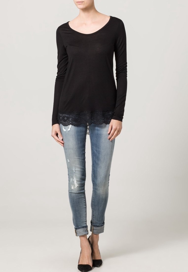 Top negro de manga larga con un dobladillo de encaje, combinado con jeans de un azul claro con un diseño desgastado, puños doblados y tacones negros.
