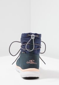 Botín azul marino con cuello acolchado, suela de goma y cierre de cordones. Logo en la parte trasera en coral claro. Parte superior de tela texturizada.