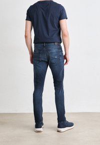 Blå denimjeans med slim fit, med bakfickor och en märkesläderlapp i midjan. Bärs med en marinblå t-shirt och avslappnade skor.