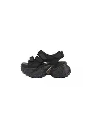 Sandale sportive noire avec une semelle épaisse crantée, plusieurs sangles ajustables et un accent argenté sur le côté extérieur de la semelle.