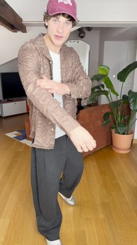 Camisa button-up castanha com um padrão ondulado, usada sobre uma camisa branca, combinada com calças largas pretas e sapatos prateados.