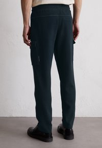 Pantalons cargo marine avec une taille élastique, dotés de poches latérales et d'un tissu texturé. Le design est fuselé au niveau des chevilles.