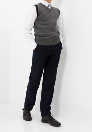 Gilet grigio in lana sopra una camicia bianca, abbinato a pantaloni scuri blu navy e scarpe in pelle nera. Il gilet ha un collo a V e bordi a costine.