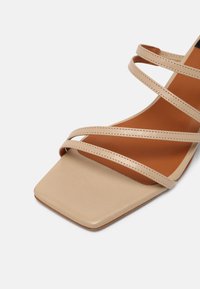Sandale beige à bout ouvert avec avant carré, trois fines brides et semelle intérieure marron clair sur fond blanc.