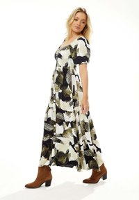 Maxi dress in black, white, and olive green leaf pattern; puff sleeves, button detail, and flowing fabric, paired with brown ankle boots.