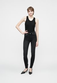 Top preto canelado combinado com jeans skinny pretos de cintura alta. O conjunto é complementado por sapatos de salto agudo pretos. Design simples, sem padrões.