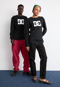 Sorte langærmede skjorter med hvid DC-logo, parret med røde baggy bukser og sorte jeans. Skoene inkluderer sorte platform-sko og nittede flade sko.