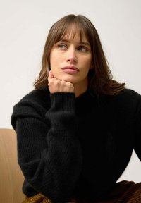 Czarny sweter z dzianiny o wysokiej szyi i ściągaczach. Miękka tekstura i luźny krój, nałożony na wzorzysty strój.