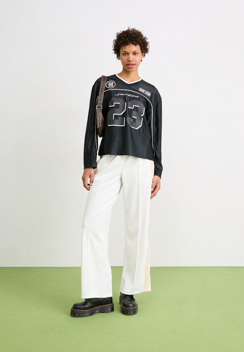 Camisa negra de manga larga con gran impresión blanca del "23" y acentos de logo; combinada con pantalones amplios blancos y botas de plataforma negras gruesas.