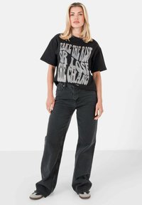 Camiseta gráfica negra con letras blancas en negrita, combinada con pantalones negros de pierna ancha. El conjunto presenta un ajuste relajado y está hecho de material de algodón.