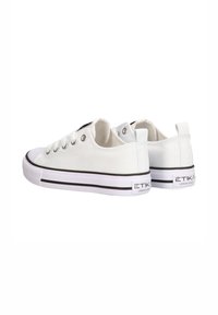 Zapatillas de lona blancas con acentos en negro, punta redonda, cinco ojales de metal, suela de goma y logo de la marca en el talón. Diseño clásico de corte bajo.