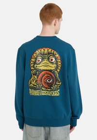 Φούτερ σε χρώμα τυρκουάζ με μεγάλο, πολύχρωμο γραφικό σχεδιασμό βάτραχου και σαλιγκαριού, με παιχνιδιάρικα μάτια και ηλιακά στοιχεία στην πλάτη.