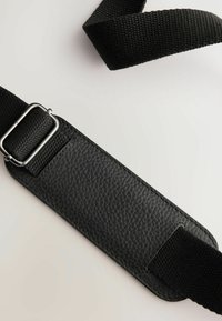 Black bag strap featuring a textured leather patch, woven fabric material, silver metal hardware, and a flat design for comfort.