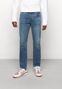 Ljust blå denimjeans med rak skärning, med femfickorsdesign och subtila sömmar. I kombination med vita sneakers och en vit sweatshirt.