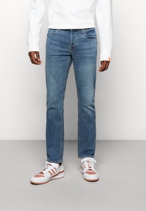 Jeans in denim azzurro chiaro con taglio dritto, caratterizzati da un design a cinque tasche e cuciture sottili. Abbinati a sneaker bianche e a una felpa bianca.