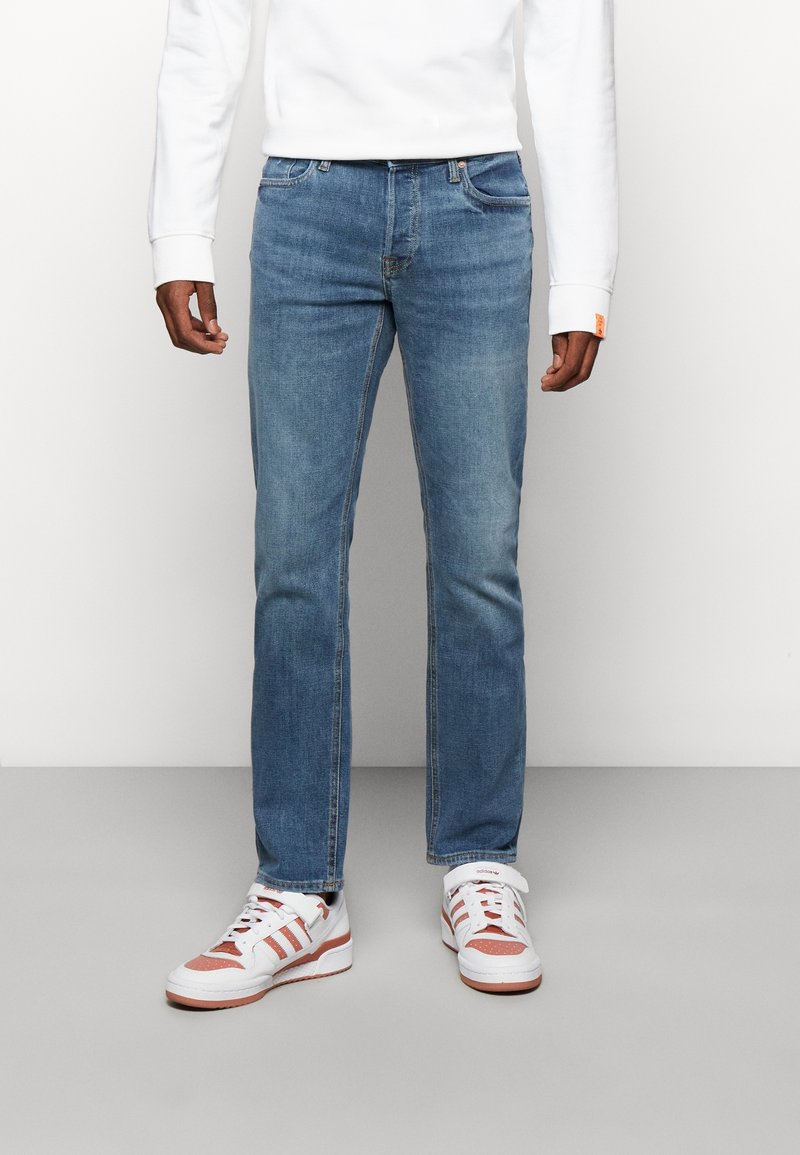 Ljust blå denimjeans med rak skärning, med femfickorsdesign och subtila sömmar. I kombination med vita sneakers och en vit sweatshirt.