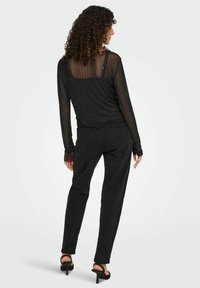 Sort langærmet top med gennemsigtig struktureret stof og prikket mønster, parret med sorte højtaljede jeans og sorte strappy hæle.