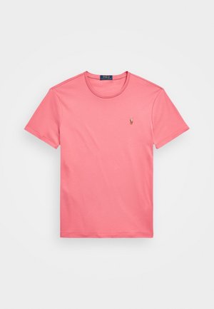 Różowa koszulka z krótkim rękawem i okrągłym dekoltem z małym haftowanym logo Polo Ralph Lauren na lewej piersi na białym tle.