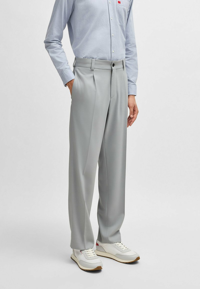 Gray tailored pants with a high waist, pleated front, and a smooth texture, paired with a light blue shirt and white sneakers.