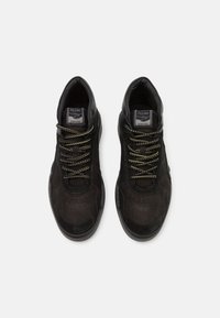 Pár černých semišových tenisek s vzorovanými tkaničkami, perforovanou špičkou a logem "Filling Pieces" na jazyku, pohled z vrchu.