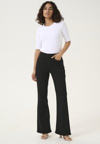 Svarta utsvängda jeans i denim, tillsammans med en åtsittande vit ribbad t-shirt med kort ärm. Outfiten har hög midja och två framfickor.