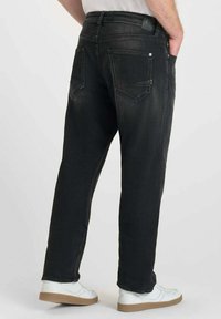 Jean en denim noir avec une coupe droite, dotés de deux poches arrière, d'un léger délavage et d'une patch en cuir à la taille. Portés avec des baskets blanches.