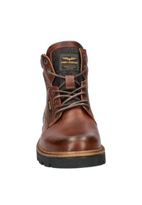 Bruine leren enkelboot met zwart stoffen paneel, ronde neus, contrasterende tan zool en metalen oogjes, met een logo patch op de tong.