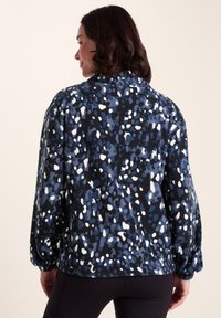 Fleece jacket with a navy base featuring a blue and white abstract pattern. Loose fit, long sleeves, and a rounded hem. Soft texture.