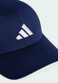 Navy blue cap made of fabric with a curved brim, featuring a white embroidered three-stripe logo on the front. Textured surface details.