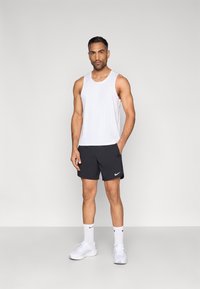 Λευκό αμάνικο τοπ και μαύρο σορτς, και τα δύο από ελαφρύ υλικό. Λευκά αθλητικά παπούτσια και κάλτσες μήκους μέχρι τον αστράγαλο ολοκληρώνουν το αθλητικό σύνολο.