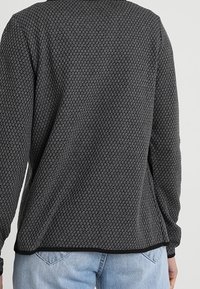 Maglione grigio scuro con texture e motivo esagonale indossato da una persona, abbinato a jeans denim azzurri, mostrato da dietro.