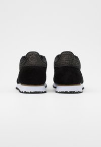Paire de baskets noires avec panneaux texturés au talon, semelles intermédiaires blanches et semelles extérieures noires à éclats blancs, vues de dos sur fond blanc.